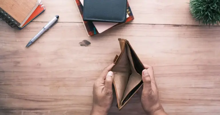 Person haelt leeres Portemonnaie ueber einem Notizbuch auf dem Schreibtisch