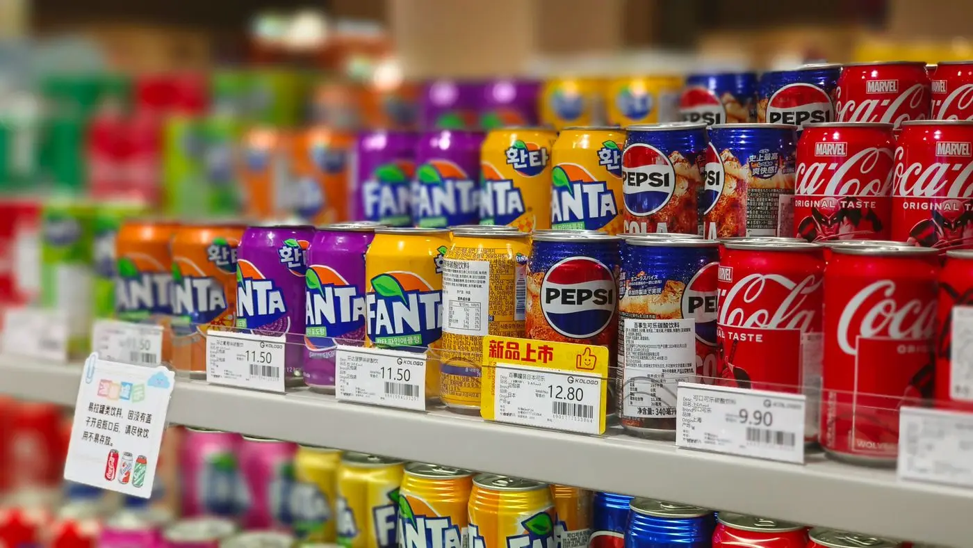 Getränkedosen im Supermarktregal mit Preisschildern — Inflation zeigt sich zuerst an den Preisen