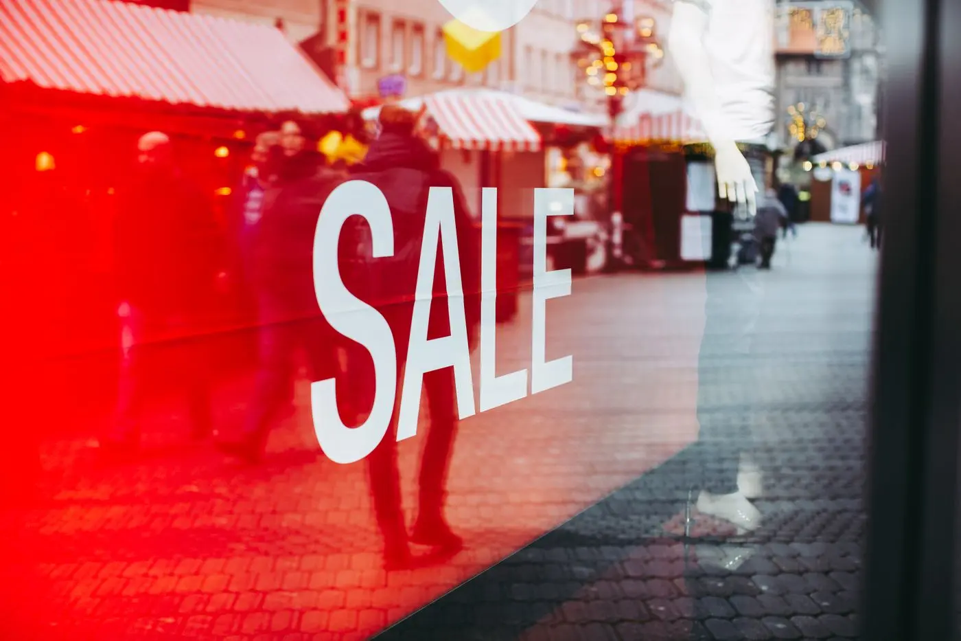 Rotes Sale-Banner in einem Schaufenster, davor Passanten — Rabattschilder erzeugen Dringlichkeit