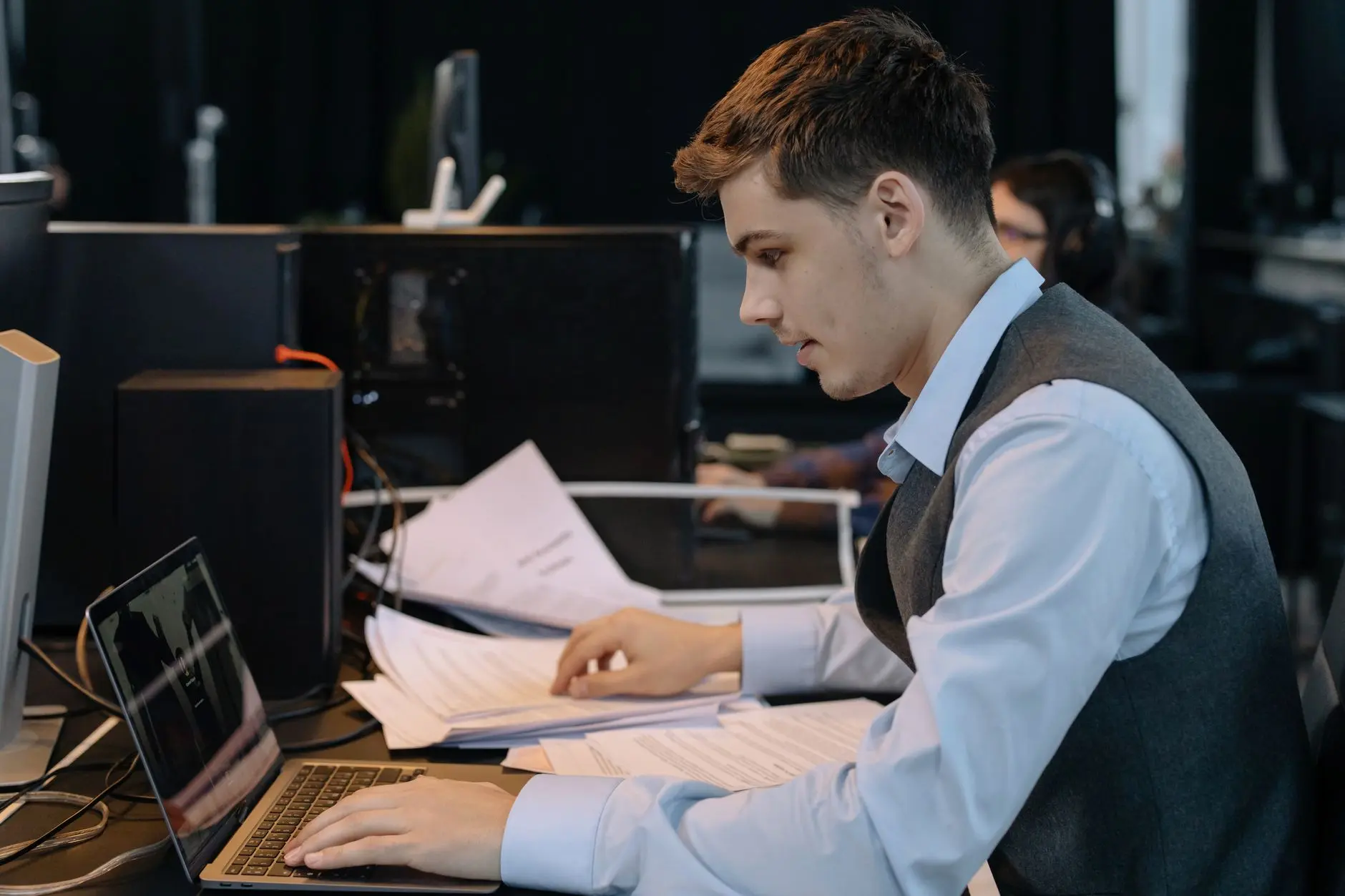 Junger Mann sitzt am Laptop und geht dabei Unterlagen auf dem Schreibtisch durch