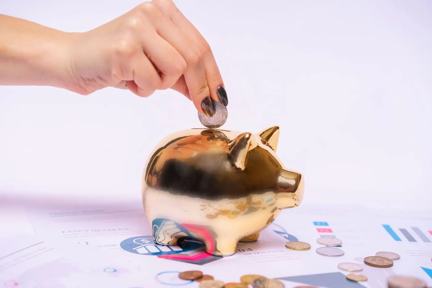 Hand steckt eine Münze in ein goldenes Sparschwein zwischen Finanzunterlagen